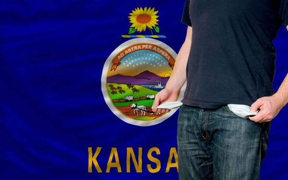 poor man showing empty pockets in front of american state of kansas flag