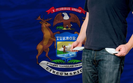 poor man showing empty pockets in front of american state of michigan flag