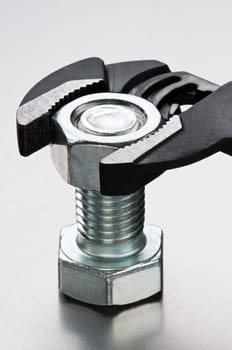 Pliers and silver bolt on metallic background close up