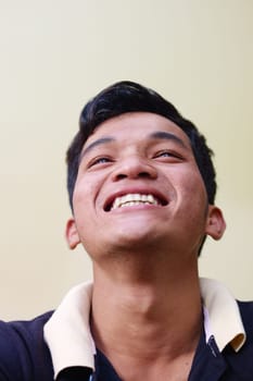Portrait of happy young asian man smiling and looking up against yellow wall. Copy space