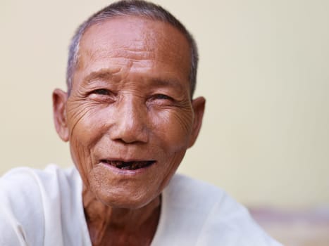 Portrait of happy senior asian man with dental problems laughing and looking at camera against yellow wall