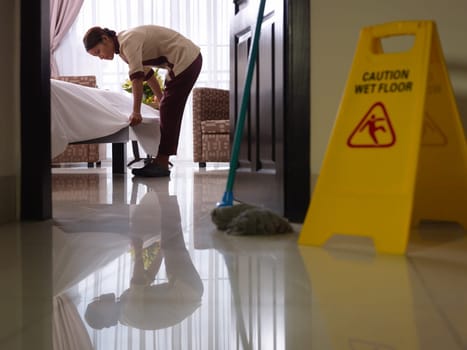 Asian maid tidying up bed and cleaning luxury hotel room