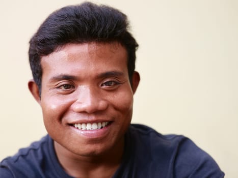 Portrait of happy young asian man smiling and looking at camera against yellow wall. Copy space