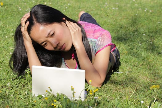 Young pretty girl working on laptop outdoor, lying on grass