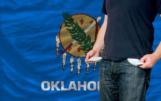 poor man showing empty pockets in front of american state of oklahoma flag