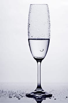Wet champagne glass with drops in contrast against a white background with reflection on the bottom