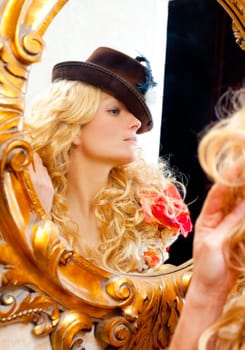fashion blond woman with hat looking in baroque golden frame mirror