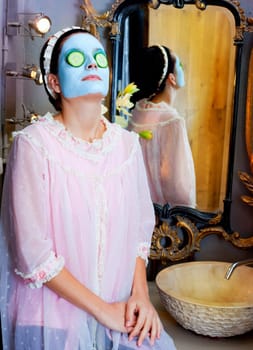 Funny housewife beauty green clay mask and cucumber at the mirror