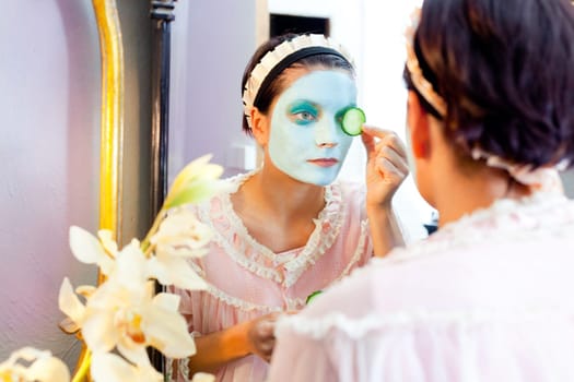 Funny housewife beauty green clay mask and cucumber at the mirror
