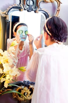 Funny housewife beauty green clay mask and cucumber at the mirror