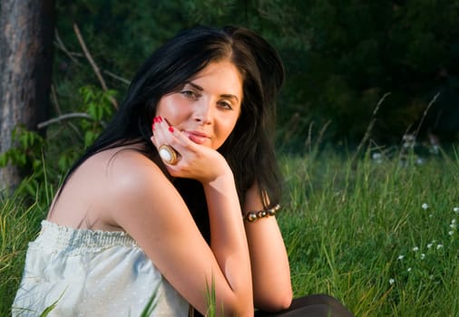 Young black-haired woman sitting in the grass to the side of the camera and looking at the camera