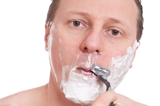 A European with shaving cream shaves with a razor