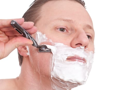 A man with shaving cream on his face shaving wet with a razor