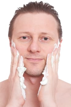 A smiling man smears shaving cream on his facial cheeks