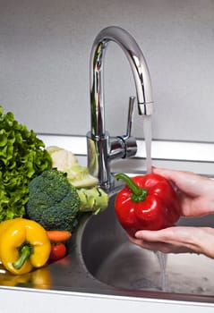 Woman washing red pepper in kitchen close up
