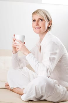Young woman sitting on sofa, drinking coffee