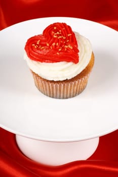 Fancy Valentine&#039 s day cupcake frosted with a red heart shape on a white tray over a red background. With copyspace.