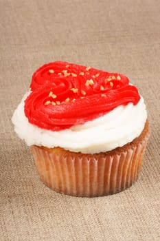 Fancy Valentine&#039 s day cupcake frosted with a red heart shape over a natural jute background. With copy-space