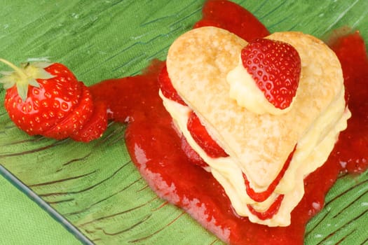 Heart shaped strawberries and custard millefeuille on a strawberry sauce, over a green background. For a sweet Valentine&#039 s Day. Selective focus.