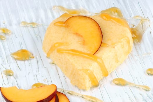 Heart shaped peach bavarian cream dessert with peach sauce and peach slices on a transparent glass plate. Selective Focus.