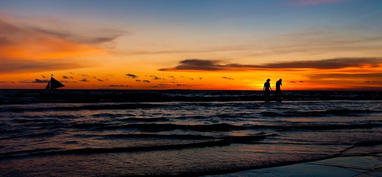 tropical beach with sailing boats and active people at sunset