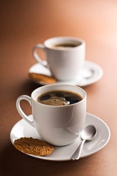 Two cups of black coffee on brown background
