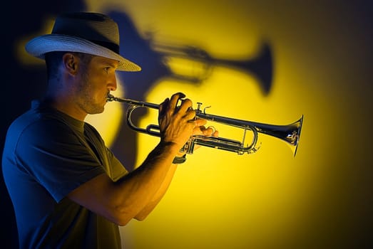 Young man playing trumpet on yellow background