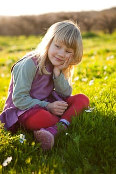 Cute little girl outdoors sitting on a green field with flowers