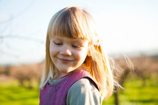 Cute little girl outdoors on a green field with flower in her hair