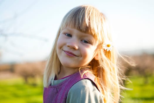 Cute little girl outdoors on a green field with flower in her hair