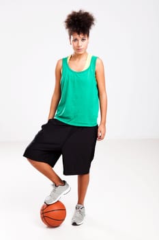 Athletic woman standing with a basketball under her foot. Studio shot.