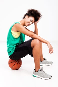 Athletic woman sitting on a basketball. Studio shot.