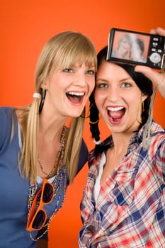 Two young woman friends taking picture with camera orange background