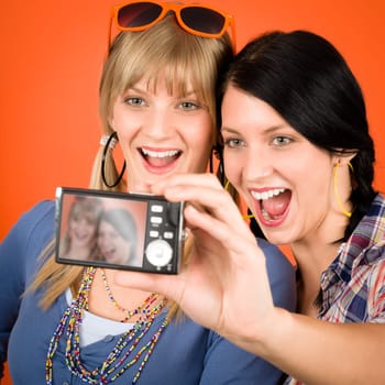Two young woman friends taking picture with camera orange background