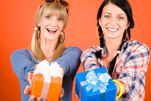 Two young woman friends hold party presents smiling orange background