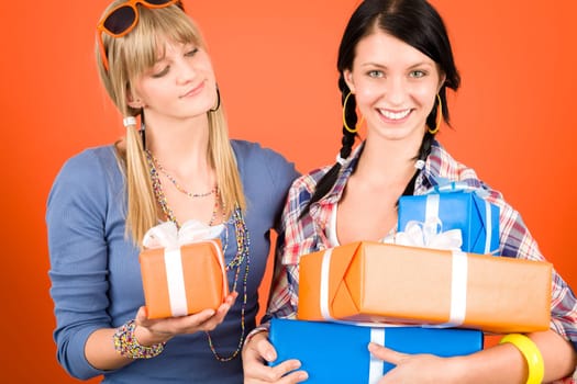 Two young woman friends hold party presents smiling orange background