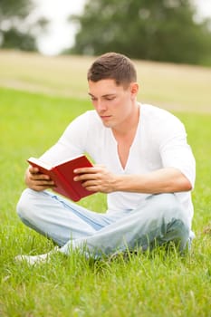Young man with a book in a meadow