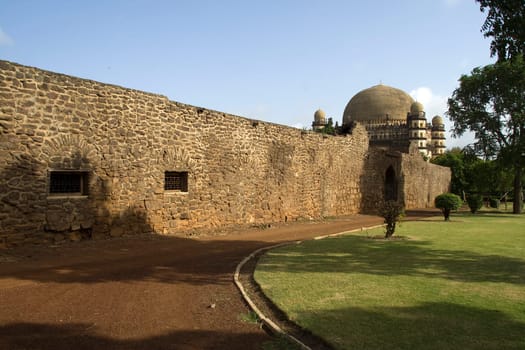Lengthy stone wall partially hides the mammoth monument Gol Gumbaz in Bijapur, Karnataka, India, Asia