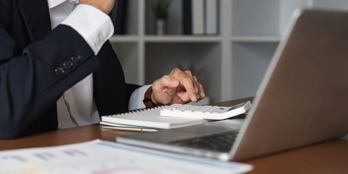 A close-up view of an elderly businessman calculating figures while taking notes, demonstrating financial management skills.