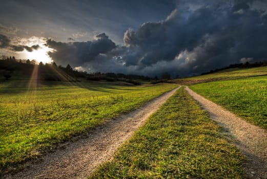 Country Road with sun shining through Rainy Clouds