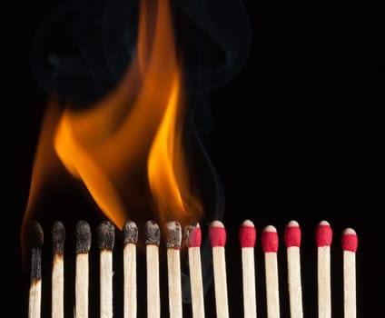 A line of red safety matches showing burnt out matches on the left , through burning matches, ignition, and unused ones on the right.