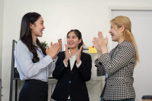 A diverse group of businesswomen applauds each other in an office, showcasing teamwork and celebrating their achievements.