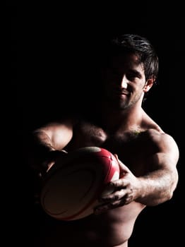 one caucasian sexy topless man portrait tossing   a rugby ball on studio black background