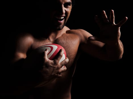 one caucasian sexy topless man portrait hugging a rugby ball on studio black background