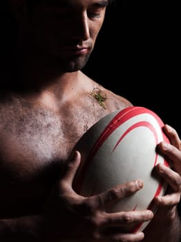 one caucasian sexy topless man portrait hugging a rugby ball on studio black background