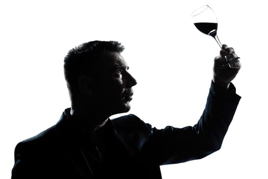 one caucasian man portrait silhouette tasting  looking at his glass of red wine in studio isolated white background