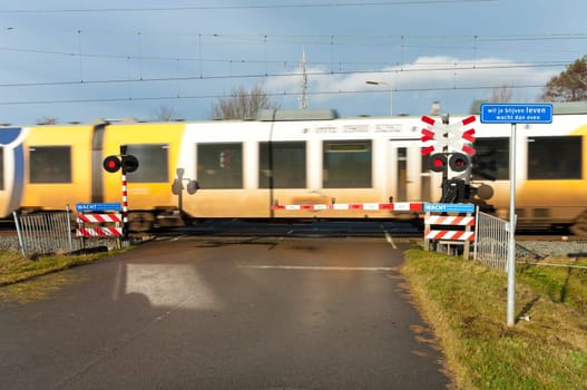 high speed train passing a secured railway crossing. The blue shield says "If you want to stay alive, you better wait a minute""."