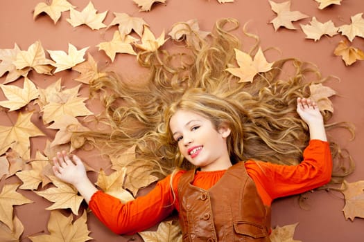 autumn fall little blond girl on dried tree leaves background and long spread hair