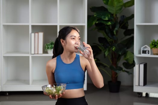 A woman takes a sip of water while holding a salad, emphasizing the importance of hydration in a healthy diet.