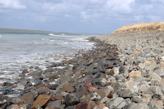 a pebbled beach on a bright day with calm sea waves splashing against the pebbles as a background